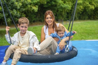 Happy family enjoying a sunny day at the playground, the mother is swinging with her two children