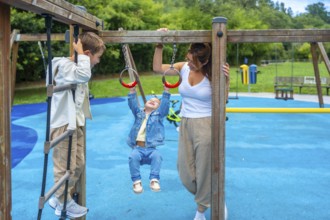 Mother watching children playing joyfully on monkey bars at the playground, fostering family