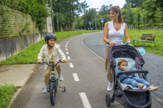 Happy mother walking with her two children, one riding a bicycle with training wheels and the other