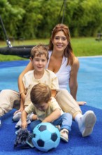 Mother and her two sons are sitting on a playground's blue rubberized surface, enjoying quality