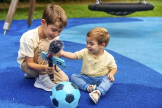 Two brothers playing as videobloggers in the playground, capturing fun moments with their phone and