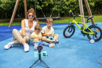Influencer mother recording a video with her two sons at playground using a smartphone and
