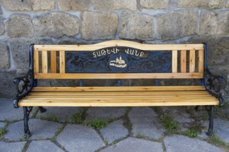 Wooden bench with decorative metal engravings in a paved area, wooden and cast iron bench, Tatev