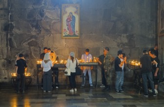 People gather in a church praying, surrounded by burning candles and murals, in a thoughtful mood,