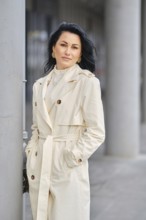 An urban portrait of a woman in a cream trench coat . The scene showcases autumn weather with a