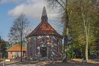 Brick chapel with pointed roof and roof turret, surrounded by autumn trees under a blue sky,