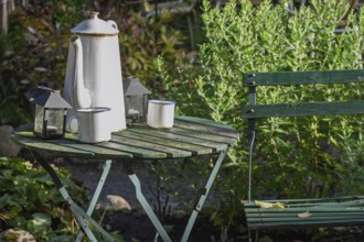 A green garden table with white enamel pot and cups surrounded by plants, Münsterland, North