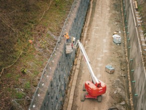Construction workers on a lift attach a net to a steep slope, construction of the Hermann Hesse