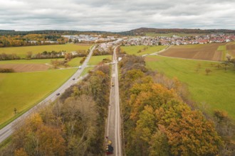 Wide landscape with roads, autumn fields and a village in the background under overcast sky,