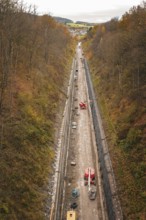 A long construction site in a wooded valley in autumn with heavy construction equipment and