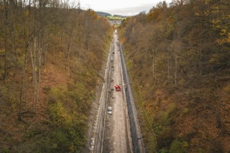 Aerial view of a construction site in an autumnal forest, with a long area of soil between steep
