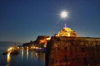 Old fortress, illuminated fortress at night with cross and starry sky over quiet harbor, UNESCO
