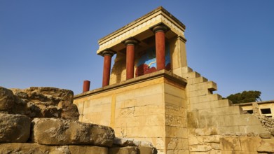 Ancient ruins with typical red Minoan columns and wall painting, under blue sky on the island of