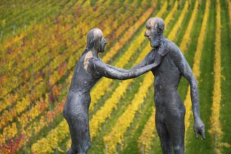 Sculpture of two people in front of colorful vines in autumn, emphasized by artistic