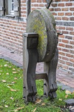 Old whetstone on wooden stand surrounded by grass and brick buildings, Münsterland, North