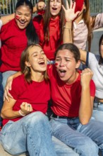 Group of enthusiastic women wearing red shirts and face paint, celebrating with open mouths and