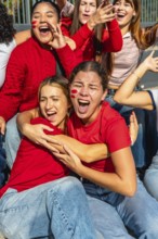 Group of excited young women wearing red, cheering loudly with face paint on their cheeks,