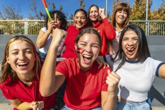 Diverse group of young women cheering loudly in a stadium, faces painted and fists raised,