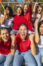 Group of excited young women with face paint and red clothing cheering passionately during a