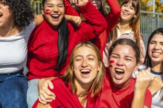 Group of enthusiastic young women friends celebrating together at a stadium, wearing red clothing