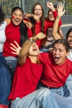 Diverse young women in red t shirts with face paint cheering and celebrating together at a stadium,