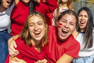 Group of excited young women wearing red shirts and face paint, screaming and cheering while
