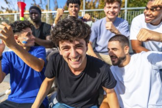 Young diverse male friends cheering in a sunlit stadium, celebrating their team with smiles,