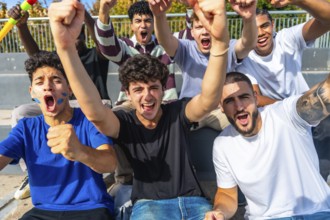 Excited multiethnic male friends cheering and raising fists in outdoor stadium, standing together