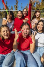 Group of excited young women friends watching a sport game, wearing red shirts and face paint,