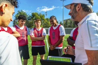 Soccer coach discussing game strategy and explaining tactics on a digital tablet with a group of