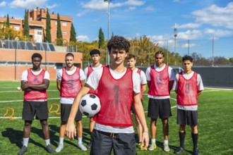 Diverse group of young male soccer players wearing red bibs and shorts, standing confidently on a