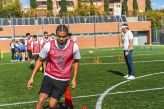 Young male soccer player in a red bib practices drills on green artificial turf with teammates