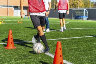 Football player practicing drills with ball and cones on artificial green turf, focused on