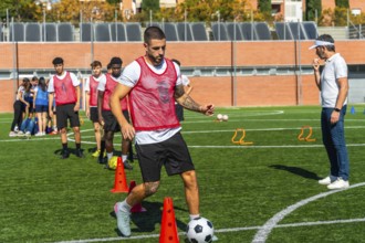 Soccer player in a red bib training on a green artificial turf field, dribbling a football around