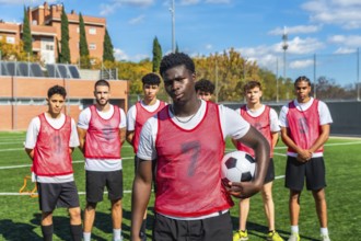 Young multi ethnic men's soccer team in red bibs and white shirts standing on a sunny green pitch,