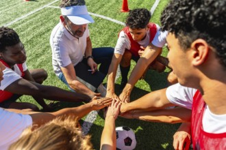 Soccer coach and a diverse group of young male players are huddling on a green artificial turf