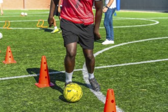 Young player actively training and practicing soccer drills, dribbling the ball around orange cones