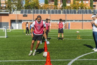 Young men in red vests are performing agility drills with cones and soccer balls on a green