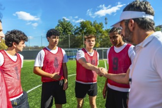 Coach wearing a visor and whistle shaking hands with a young male soccer player on a green football
