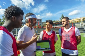 Soccer coach discussing game strategy with diverse football players on a sunny training field,