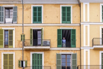 Senior citizen standing and looking out from open window in an old apartment building with