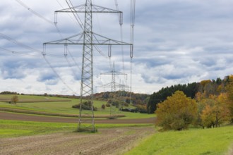 Power poles in a field under cloudy sky and autumn trees, Swabian Jura, Baden-Württemberg, Germany