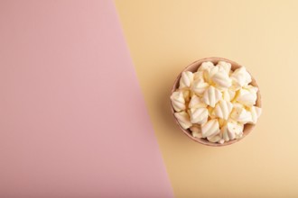 Orange and pink marshmallow in ceramic bowl on pink and orange pastel paper background, top view,