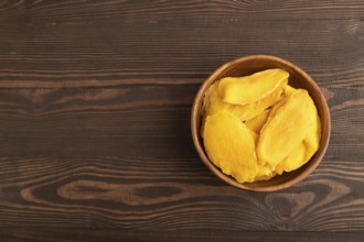 Dried Mango in wooden bowl on brown wooden background. Top view, copy space, flat lay. healthy