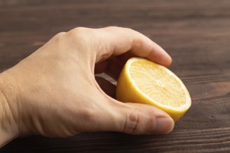 Yellow Lemon Cut in half with hand on brown wooden background. Side view, close up. healthy food,
