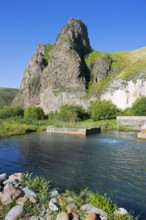 Clear water flows through a green landscape, framed by majestic, sunlit rocks, hot spring, Vorotan,