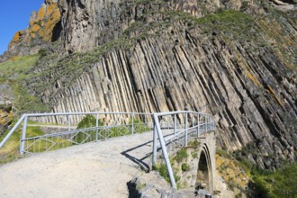 A narrow path with railing leads over a stone bridge, surrounded by unique vertical rock