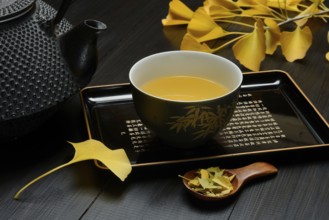 Ginkgo tea in tea bowl and ginkgo leaf, tea leaves in a spoon, ginkgo biloba