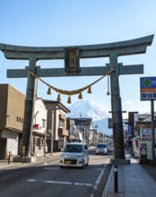 Large torii gate on above a street, street scene, in the back volcano Mt. Fuji, Fujiyoshida,