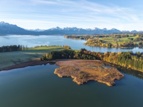 Clear lake, surrounded by autumn trees, with alpine peaks on the horizon under clear sky,